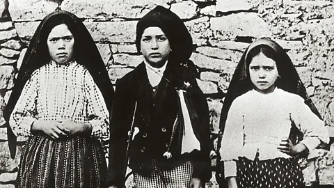 A black-and-white photograph of three young girls stood against a dry stone wall (Credit: Getty Images)