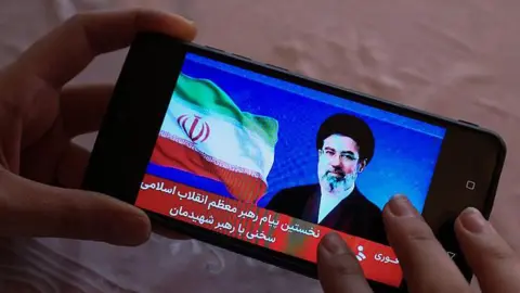 AFP via Getty Images Hands holding a mobile phone showing an image of Iran
