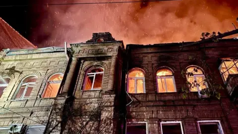 Dnipropetrovsk Regional State Administration A building damaged and on fire in Dnipro, Ukraine, in April 2026. The roof appears to have caved in and the windows are lit by fire, as is the night sky.